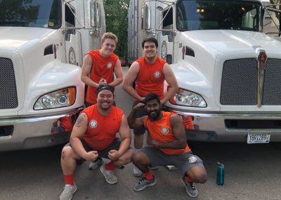 Four Muscle Movers flexing and smiling in front of a moving truck